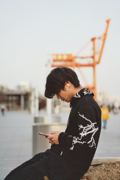 man sitting by water using earphones